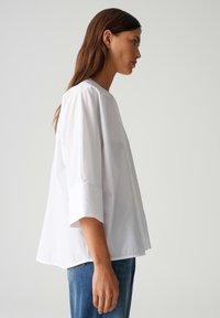 Witte, lichtgewicht blouse met een ronde halslijn en 3/4 mouwen. Kenmerkt zich door een losse pasvorm en subtiele glans, gecombineerd met blauwe denim jeans.