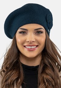 Sötétkék gyapjú baret, feltekert virágmotívummal, lekerekített formával és textúrált felülettel, amely szoros illeszkedésre van tervezve a fejre.