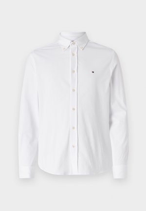 Camisa de botones de manga larga blanca hecha de algodón. Presenta un cuello tipo punta y un pequeño logotipo en el lado izquierdo del pecho. Dobladillo redondeado y puños abotonados.