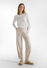 Maglione beige chiaro a maniche lunghe abbinato a pantaloni da lounge testurizzati color crema con vita elastica e cordino. Footwear marrone da indossare senza lacci.