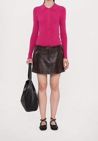 Cardigan long à rayures fuchsia, jupe mini en cuir marron avec poches zippées, sac à main noir et chaussures noires à pois blancs.