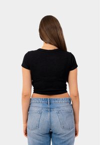 Černý krátký rukávový crop top s kulatým výstřihem, kombinovaný se světle modrými džíny s vysokým pasem a viditelnými zadními kapsami. Hladká textura.