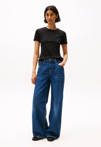 Zwarte katoenen t-shirt met korte mouwen, gecombineerd met wijde blauwe denim jeans. De jeans hebben een klassiek vijf-pocket ontwerp en riemlussen.