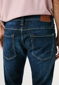 Tmavomodré džínsy z denimu s rovnýms strihom, kontrastným žltým prešívaním a dvoma zadnými vreckami s výrazným uhlovým dizajnom.