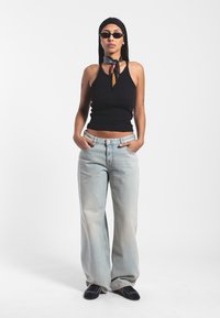Schwarzes geripptes Tanktop, hellblaue hochtaillierte weitgeschnittene Jeans, schwarze Schuhe, Seidenschal um den Hals gebunden, Sonnenbrille, minimale Accessoires.