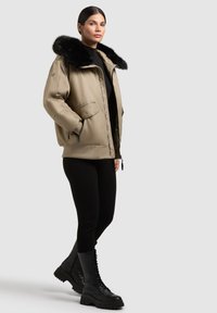 Smėlio spalvos pūkinė striukė su juodu pūkų apvadu, su užtrauktuku ir šoninėmis kišenėmis. Juodos leginsai ir bateliai su raišteliais puikiai papildo įvaizdį.