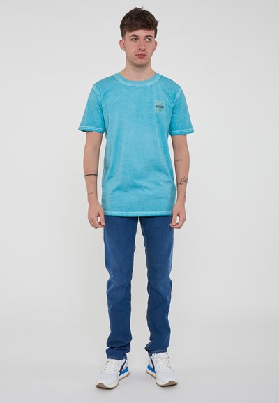T-shirt in cotone azzurro con maniche corte, collo a giro e taschino sul petto. Abbinato a jeans blu e sneakers bianche con dettagli blu.