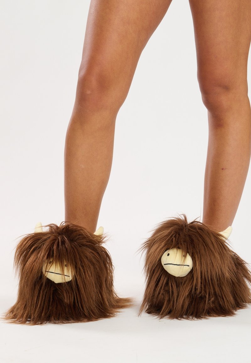 Chaussons en fourrure brune ornés de créatures au visage jaune, avec de longs cheveux et de petites cornes, conçus pour un usage intérieur.