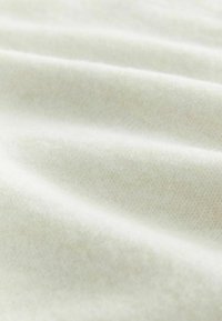 Nahaufnahme eines weichen, cremefarbenen Strickstoffs mit sanften Falten und sichtbarer feiner Garnstruktur.