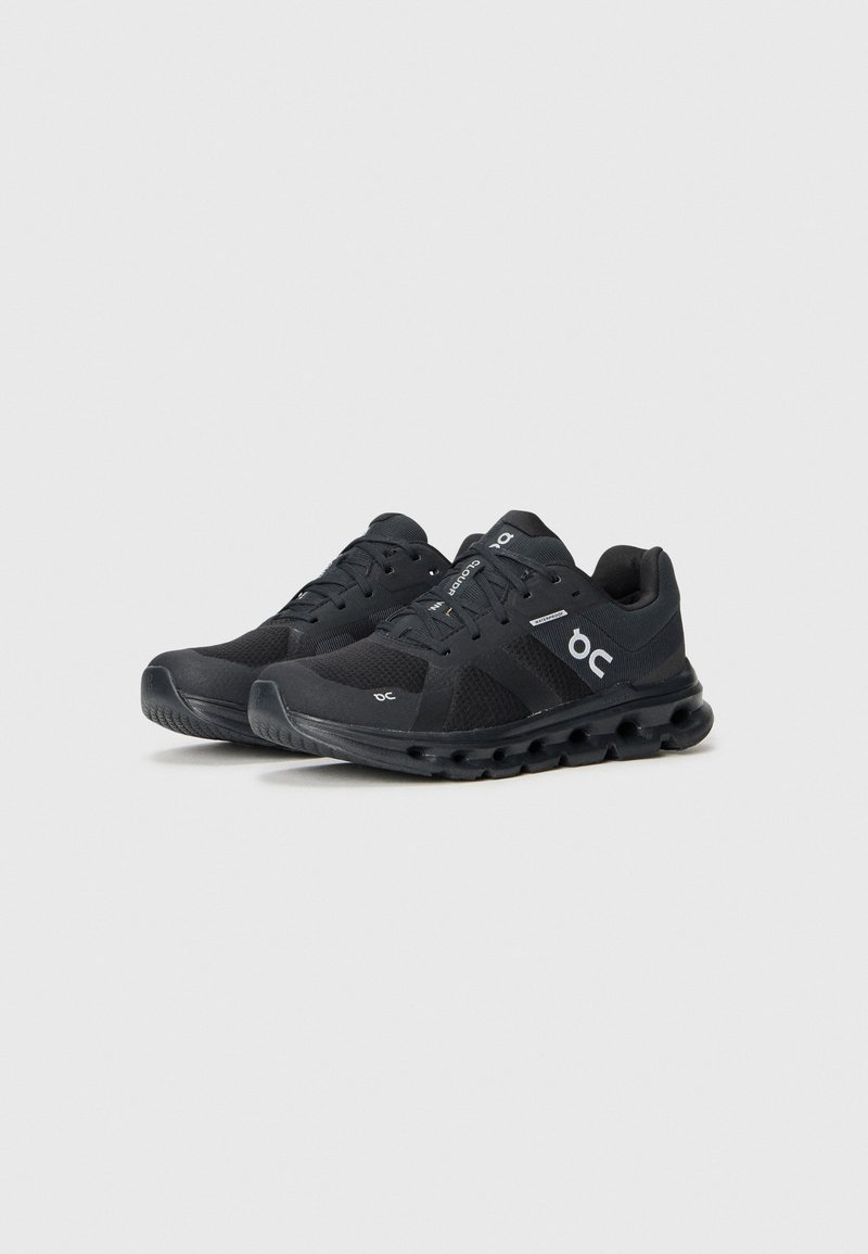 Las zapatillas de correr negras cuentan con una parte superior de malla, un collar acolchado y una suela con amortiguación con acentos circulares, diseñadas para ofrecer comodidad y rendimiento.