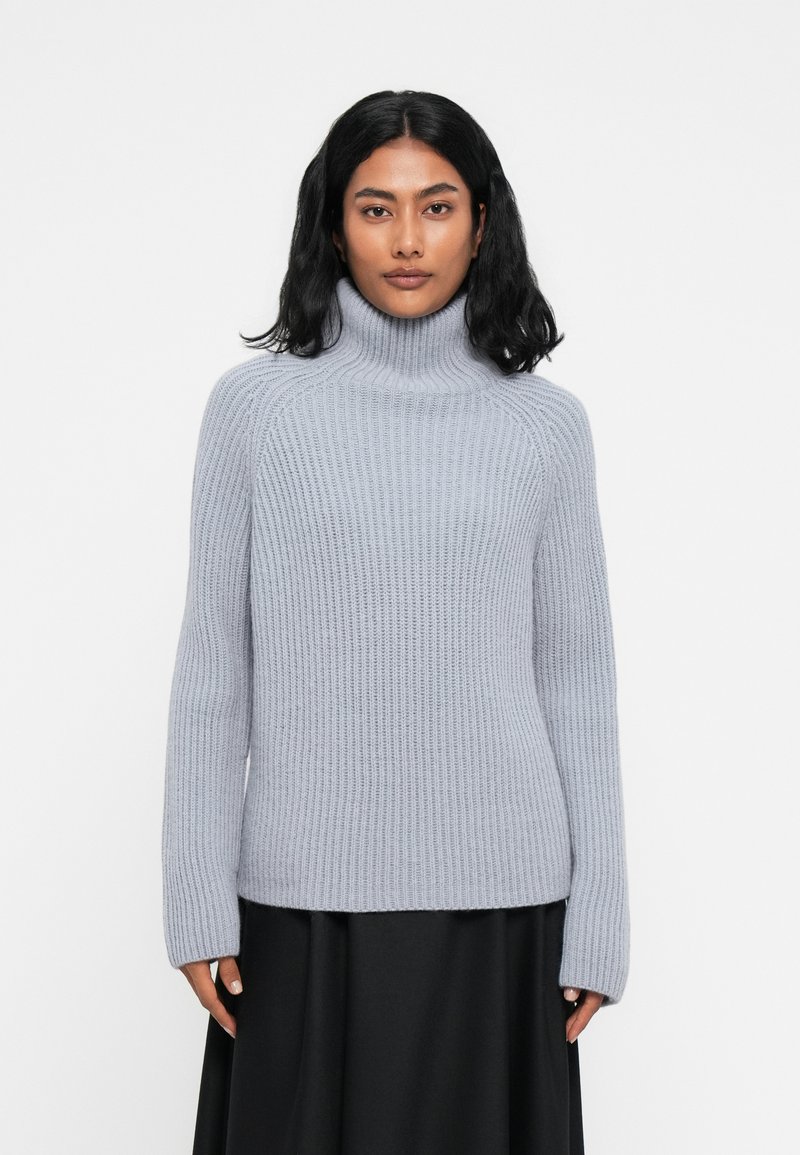 Maglione a collo alto grigio chiaro realizzato in materiale a coste, con maniche lunghe e una silhouette leggermente aderente. Senza motivi o accenti.