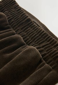 Brauner Stoff mit strukturiertem Rippendesign, das geraffte Abschnitte aufweist. Weiches, warmes Material in einem reichen, dunklen Farbton.