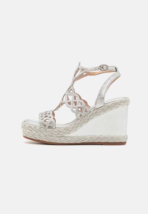 Sandales en argent avec des motifs découpés complexes, une bande ajustable à la cheville et une plate-forme en espadrille tissée.