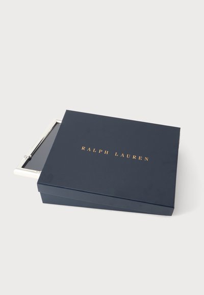 Κλειστό σκούρο μπλε κουτί Ralph Lauren με χρυσά γράμματα, μερικώς ανοιχτό για να αποκαλύψει ένα ορθογώνιο αντικείμενο με ασημένιο περίγραμμα μέσα.