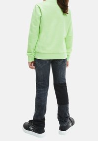 Zelená mikina s žebrovanými manžetami, doplněná tmavě šedými džíny s kontrastními záplatami. Černé tenisky s bílými podrážkami a logem.