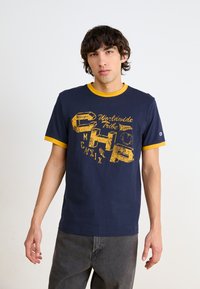 Marineblaue Baumwoll-T-Shirt mit gelbem geripptem Kragen und grafischem Druck mit gelbem Text. Kurze Ärmel und lockere Passform.