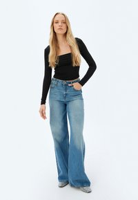Zwarte, aangesloten top met lange mouwen, gecombineerd met lichtblauwe flared jeans. De jeans hebben een vervaagde afwerking en een ontspannen silhouet.