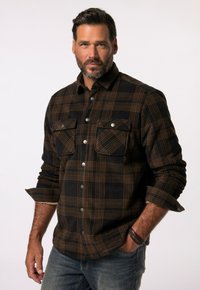 Camisa de franela a cuadros en negro y marrón con dos bolsillos en el pecho y botones plateados, con una tela texturizada y mangas arremangadas.
