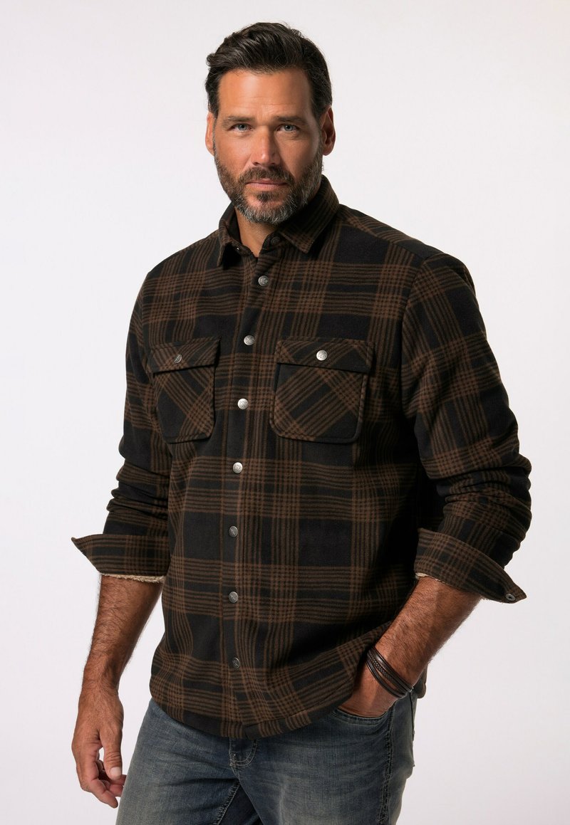Camisa de franela a cuadros en negro y marrón con dos bolsillos en el pecho y botones plateados, con una tela texturizada y mangas arremangadas.
