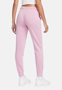 Ljusrosa sweatpants tillverkade av mjukt tyg, med elastisk midja, sidofickor och avsmalnande muddar, kombinerat med vita sneakers.