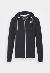 Černá mikina na zip z bavlněné směsi. Má bílý zip, stahovací šňůrky a logo Nike na levé horní straně hrudi.