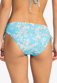 Kwiatowe majtki od bikini w jasnoniebieskim kolorze z białymi i brązowymi wzorami kwiatowymi. Posiada regulowane wiązania po bokach, umożliwiające dostosowanie dopasowania.