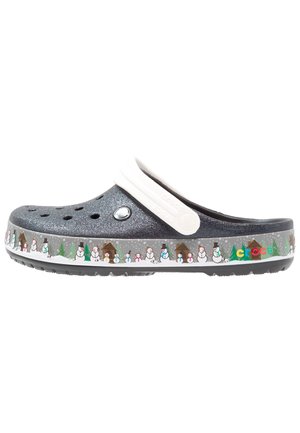 Ciemnoszare błyszczące chodaki Crocs z białym paskiem, ozdobione bałwankami, drzewami i chatkami wzdłuż krawędzi podeszwy.