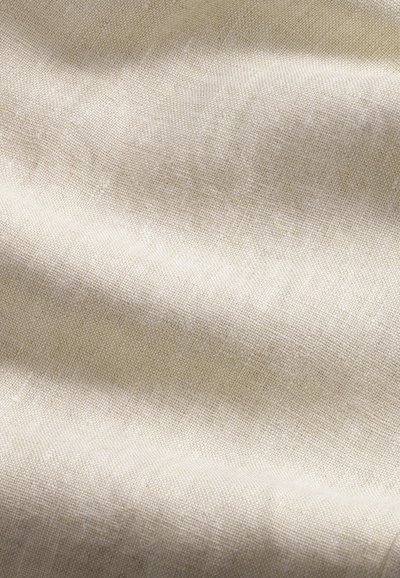 Tessuto beige intrecciato con trama visibile e onde sottili che creano variazioni di luce e ombra sulla superficie.