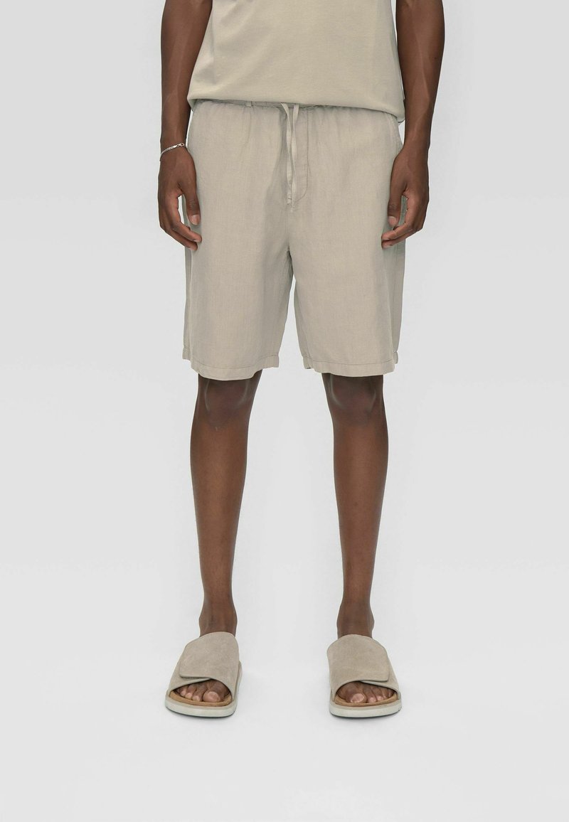 Shorts en lin beige clair avec taille élastique, cordon de serrage à l'avant et revers roulés. Associés à des sandales à enfiler assorties dans une teinte similaire.