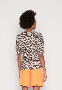 Blusa com padrão de zebra castanho e creme, com mangas bufantes, fecho de botão nas costas e textura suave, combinada com calções laranja brilhante.