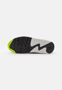 Talpa de sneaker Nike cu o bază din cauciuc negru, secțiuni texturate de culoare gri și un accent verde vibrant. Brandingul notabil și modelul de profunzime sunt vizibile.