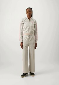 Γκρι σετ φόρμας που περιλαμβάνει φερμουάρ μπουφάν με ροζ ρίγες, παντελόνια με ελαστική μέση και μαύρα slip-on παπούτσια. Λείος υφασμάτινος ιστός.