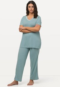 Svetle modrý loungewear set vyrobený z měkké tkaniny; top s krátkým rukávem a decentním výstřihem do V a odpovídající dlouhé kalhoty s bočními rozparky.