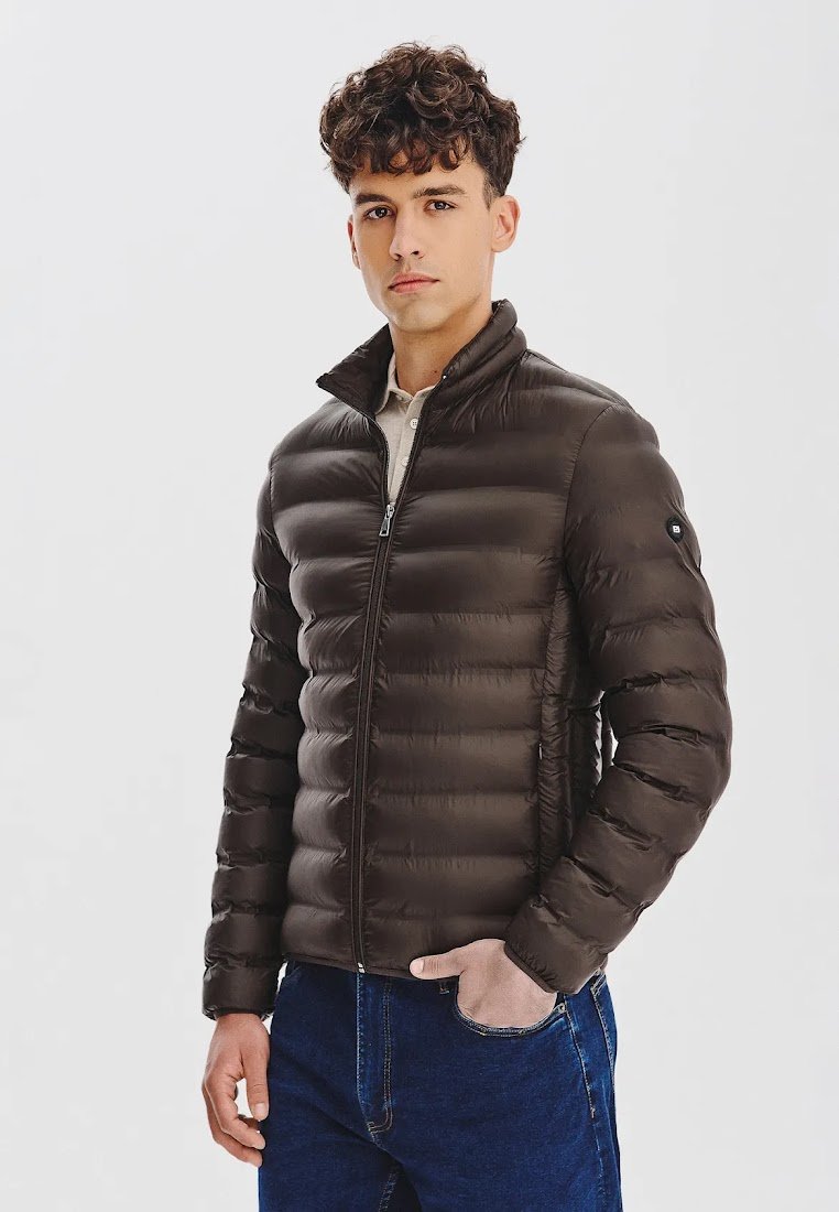 Brązowa kurtka puchowa z poziomym pikowaniem, wysoka stójka, zamek błyskawiczny z przodu i kieszeniami bocznymi, noszona na jasnej koszuli.