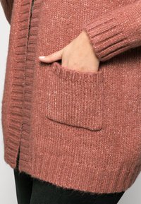Knitted cardigan in soft, rose-colored fabric with ribbed cuffs and a front pocket. Textured finish with flecks of lighter color throughout.