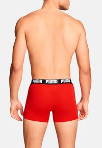 Rote Boxershorts mit einem schwarzen elastischen Bund, der das Puma-Logo zeigt. Der Stoff wirkt glatt und dehnbar. Rückansicht sichtbar.