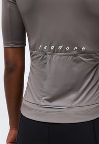 Κοντινή λήψη της πίσω πλευράς γκρι κοντομάνικου ποδηλατικού τζέρσεϊ με πίσω τσέπες και λογότυπο «isadore» πάνω από τις τσέπες.