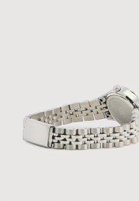 Orologio in metallo argento con bracciale a maglie, cassa circolare e corona texturizzata. Include una semplice chiusura e un retro inciso.