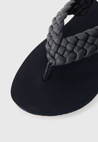 Crne kožne natikače s pletenom trakom, mekim mat đonom i oblikom koji osigurava udobno nošenje.