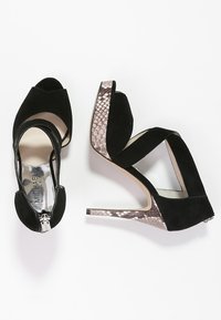 Zwarte suède high heels met een peep-toe ontwerp, voorzien van een metallic slangenhuidaccent op de hak en een rits aan de achterkant voor sluiting.
