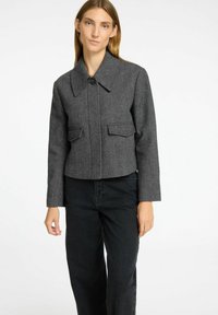 Giacca cropped a spina di pesce grigia con un ampio colletto, chiusura a bottoni e due tasche frontali, abbinata a pantaloni neri a gamba larga.