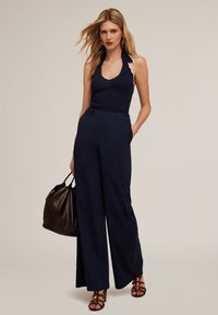 Marinblå vida byxor med hög midja, kombinerat med en marinblå ribbad halterneck-topp med scallop-dekoration. Mörkbrun handväska och sandaletter med remmar.