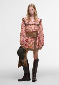 Floral-patterned pink blouse with ruffled neckline, puff sleeves, and a matching skirt. Accessories include a dark green scarf and boots.