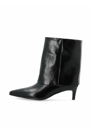 Bottine en cuir noir avec bout pointu et talon bas et fin, empeigne lisse s’étendant au-dessus de la cheville.