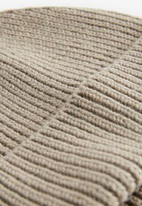 Knitted beige beanie with ribbed texture, featuring a folded cuff. Soft wool material, highlighting a warm and cozy design.