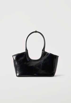 Sac à main en cuir noir brillant avec une grande poignée ovale et un logo subtil à l'avant sur un fond clair uni.