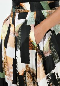 Zwarte rok met een meerkleurig abstract patroon met beige, groen en bruine accenten. Voorzien van zijzakken en een gladde stoftextuur.