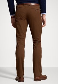 Bruna chinos med en slät textur, i slim fit-modell, bakfickor med dragkedjor och ett brunt läderbälte. Bärs tillsammans med bruna skor.