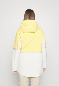 Geel-witte hoodie met een tweekleurig ontwerp, voorzien van een reflecterende strook over de rug en een zachte, gladde textuur.
