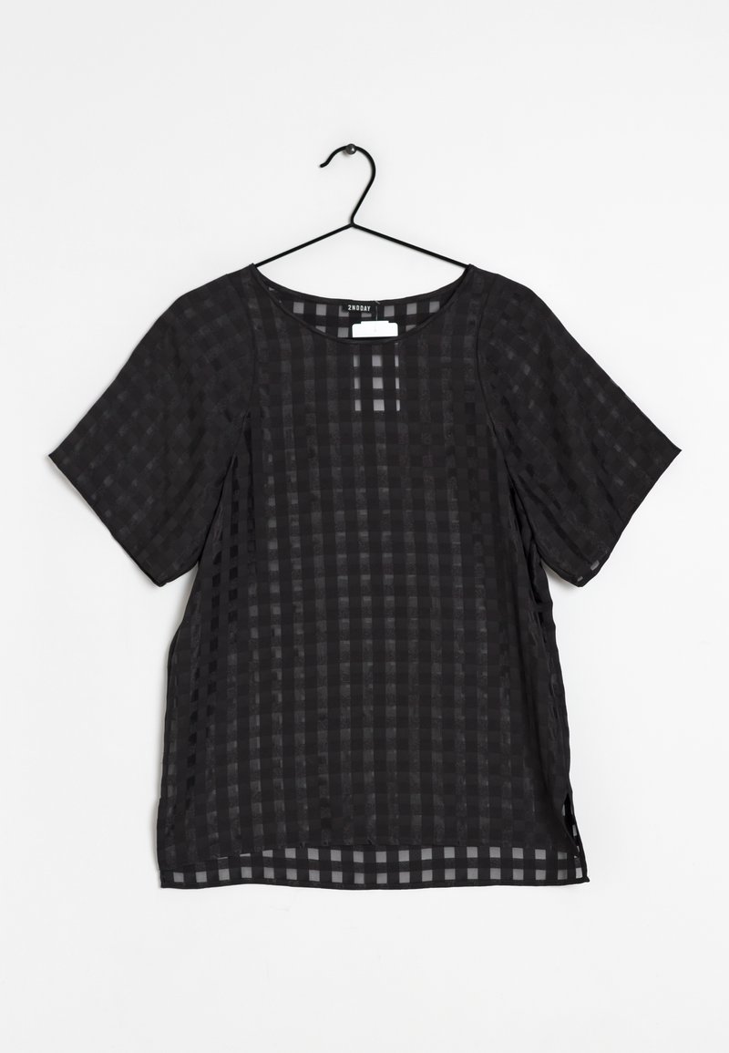 Blouse noire à manches courtes avec motif à carreaux transparent, suspendue sur un cintre noir contre un fond blanc.